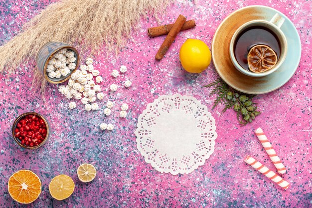 Vista superior de la taza de té con confituras dulces blancas limón y canela en superficie rosa