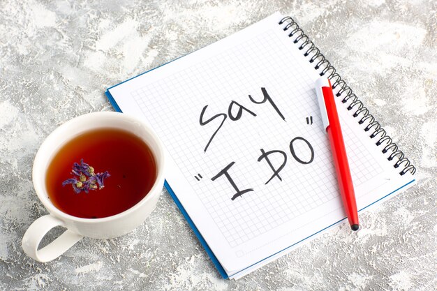 Vista superior de la taza de té con cuaderno y lápiz en el escritorio blanco