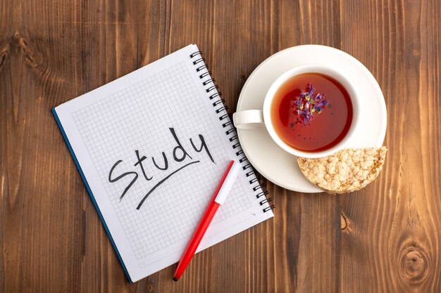 Vista superior de la taza de té con cuaderno y lápiz en el escritorio marrón