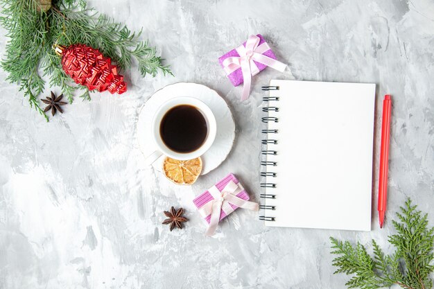 Vista superior de una taza de té, cuaderno, lápiz, pequeño regalo, árbol de Navidad, juguete sobre fondo gris