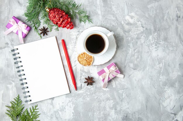 Vista superior de una taza de té, cuaderno, lápiz, pequeño regalo, árbol de Navidad, juguete sobre fondo gris