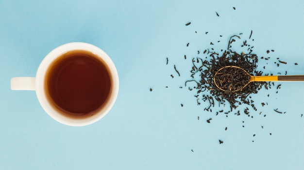 Vista superior taza de té con cuchara llena de hojas secas