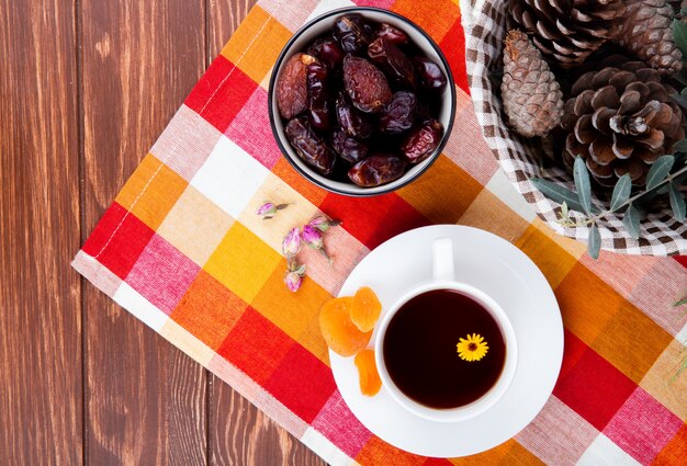 Vista superior de una taza de té con dátiles dulces secos y albaricoques sobre mantel a cuadros