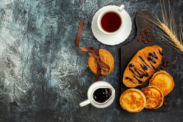 Vista superior de una taza de té y un delicioso desayuno con panqueques croisasant en mesa oscura