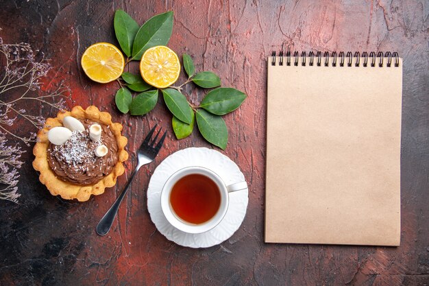 Vista superior de una taza de té con un delicioso pastelito en la mesa oscura, galleta de postre