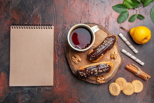 Vista superior de una taza de té con deliciosos canutillos de chocolate en un pastel de galleta dulce de mesa oscura