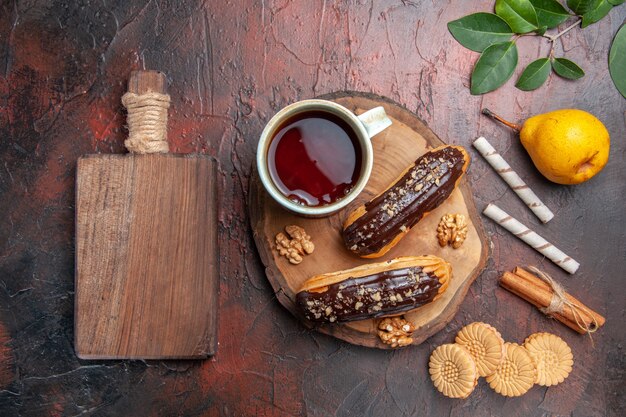 Vista superior de una taza de té con deliciosos canutillos de chocolate en un pastel de galleta dulce de mesa oscura