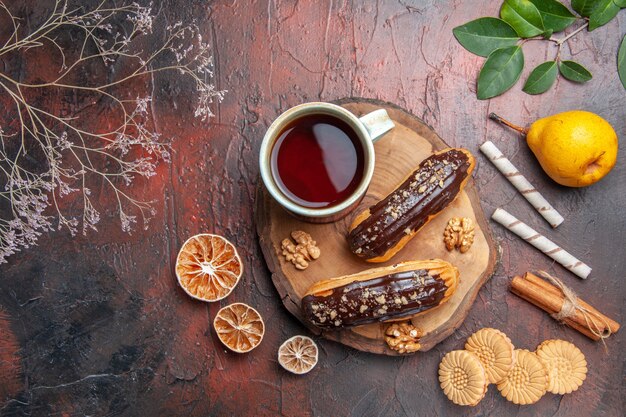 Vista superior de la taza de té con deliciosos canutillos de chocolate en postre dulce pastel de mesa oscura