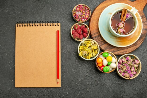 Vista superior de una taza de té con dulces y flores en el espacio oscuro