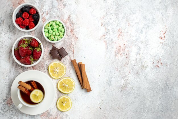 Vista superior de la taza de té con dulces y fresas sobre superficie blanca