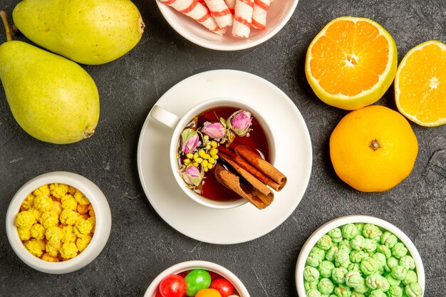 Vista superior de la taza de té con dulces y frutas frescas en el espacio gris