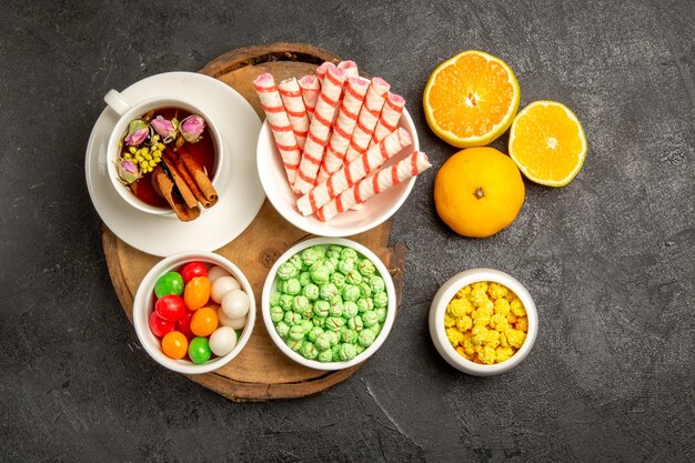 Vista superior de una taza de té con dulces y mandarinas en el espacio oscuro