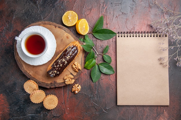 Vista superior de la taza de té con eclair y galletas en la mesa oscura pastel de galletas dulces