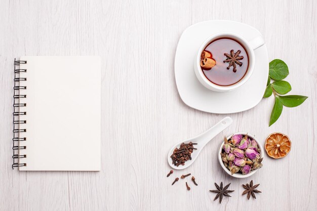 Vista superior de la taza de té con flores y bloc de notas sobre fondo blanco pastel de galletas de baya de té de frutas