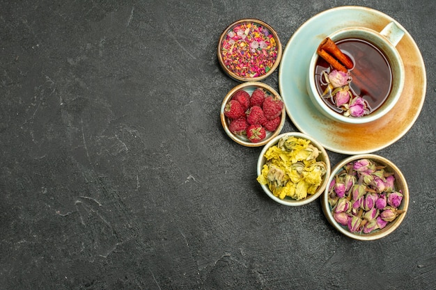 Vista superior de una taza de té con flores y frambuesas en el fondo oscuro, té, bebida de frutas, sabor a flor