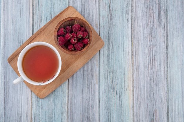 Vista superior de la taza de té con frambuesas sobre una tabla para cortar sobre una superficie gris