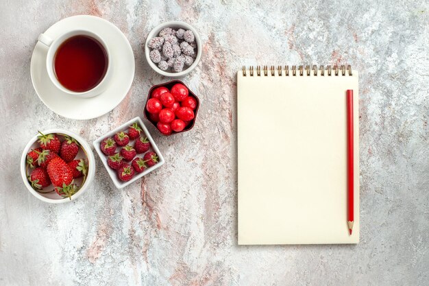 Vista superior de la taza de té con fresas y dulces sobre fondo blanco, té de bayas de frutas, azúcar dulce