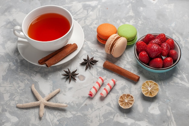 Vista superior de la taza de té con fresas frescas y macarons franceses en el escritorio blanco