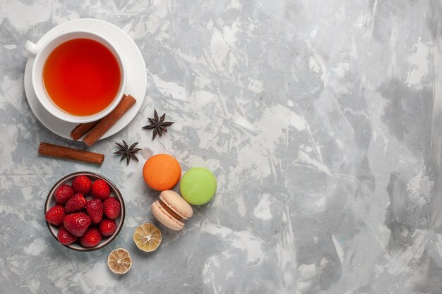 Vista superior de la taza de té con fresas frescas y macarons franceses sobre superficie blanca