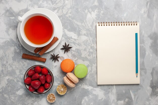 Vista superior de la taza de té con fresas frescas y macarons franceses sobre superficie blanca