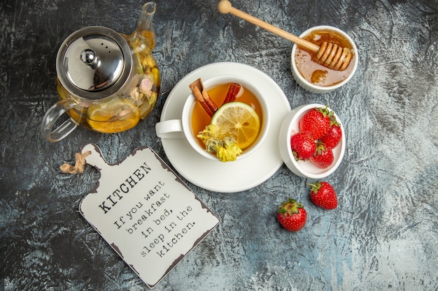 Vista superior de una taza de té con fresas y miel en la superficie oscura de la baya de té de frutas