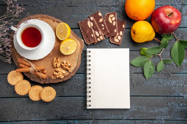 Vista superior de la taza de té con frutas y dulces en la mesa oscura