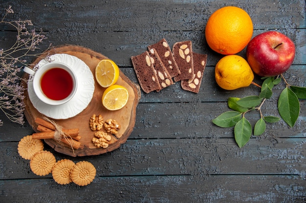 Vista superior de la taza de té con frutas y dulces en la mesa oscura