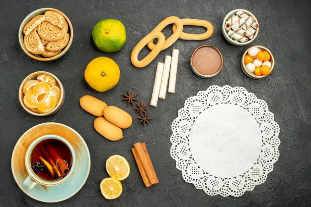 Vista superior de una taza de té con frutas y galletas en el fondo oscuro