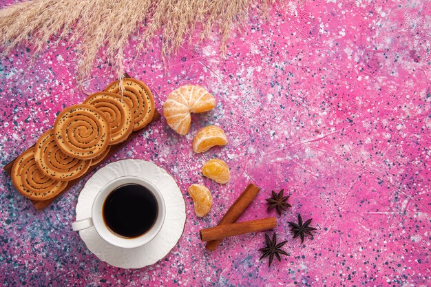 Vista superior de una taza de té con galletas de canela y mandarinas en el escritorio de color rosa claro.