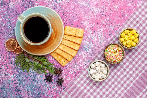 Vista superior de una taza de té con galletas y dulces en el escritorio rosa