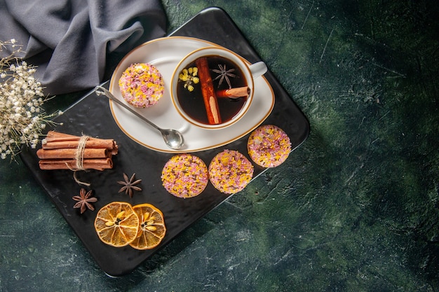 Vista superior de una taza de té con galletas dulces en un plato y bandeja sobre fondo oscuro