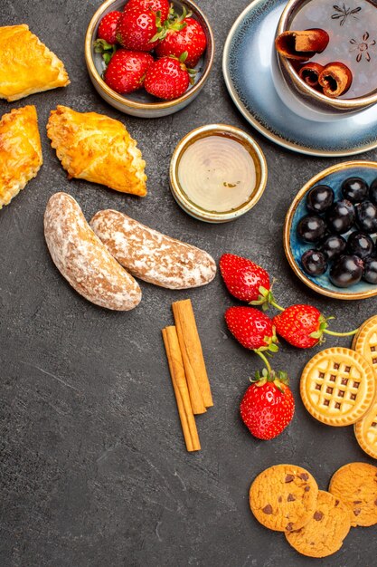 Vista superior de una taza de té con galletas y frutas en la superficie oscura pastel de frutas de galleta dulce