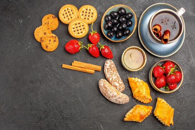 Vista superior de una taza de té con galletas y frutas en la superficie oscura pastel de frutas de galleta dulce