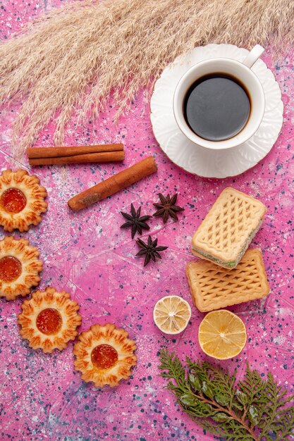 Vista superior de una taza de té con galletas y gofres en el color rosa pastel de azúcar de la galleta de la galleta del escritorio