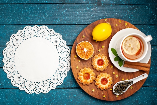 Vista superior de una taza de té con galletas y limón en el escritorio azul