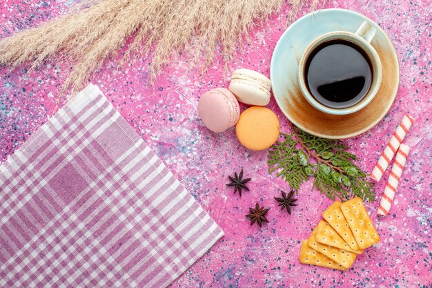 Vista superior de una taza de té con galletas y macarons en el escritorio rosa claro