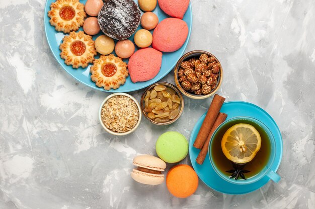 Vista superior de una taza de té con galletas macarons franceses y pasteles en la superficie blanca