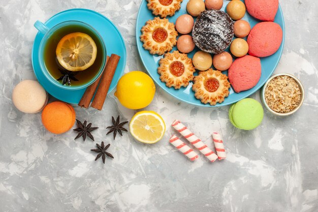 Vista superior de una taza de té con galletas macarons franceses y pasteles en la superficie blanca