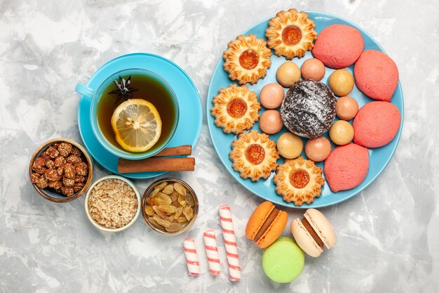 Vista superior de una taza de té con galletas macarons franceses y pasteles en la superficie blanca