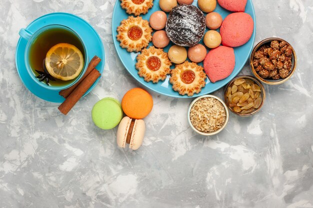 Vista superior de una taza de té con galletas macarons franceses y pasteles en la superficie blanca