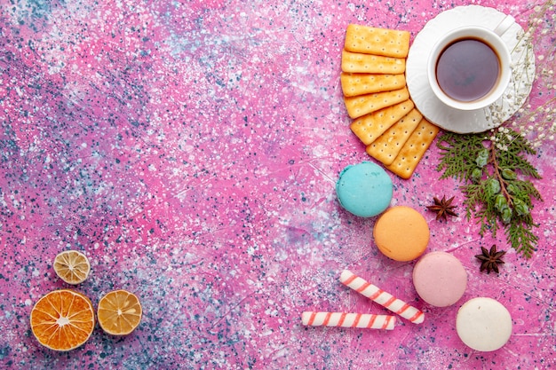 Vista superior de una taza de té con galletas y macarons franceses en la superficie rosa
