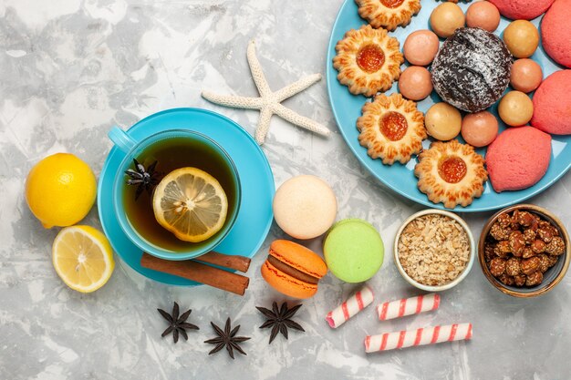 Vista superior de una taza de té con galletas macarons y pasteles en la superficie blanca