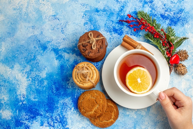 Vista superior de la taza de té en las galletas de la mano de la mujer atadas con una cuerda en el lugar de la copia de la mesa azul