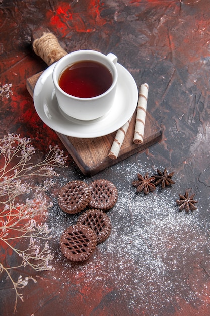 Vista superior de una taza de té con galletas en la mesa oscura