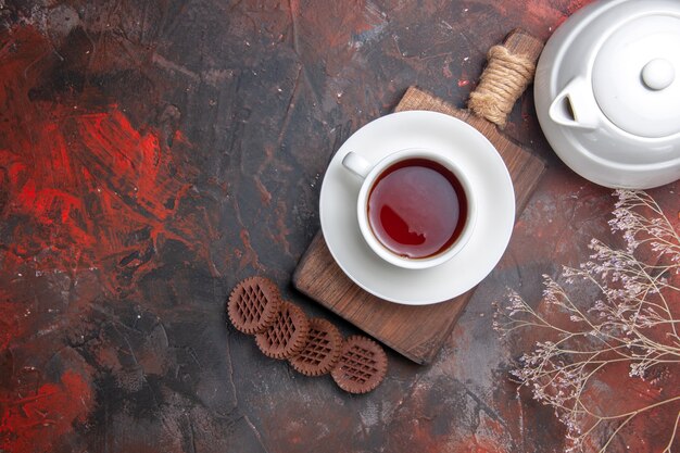 Vista superior de una taza de té con galletas en la mesa oscura