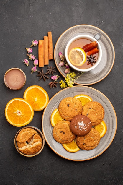 Vista superior de una taza de té con galletas y naranjas frescas en rodajas en la superficie oscura, azúcar, fruta, galleta, galleta dulce