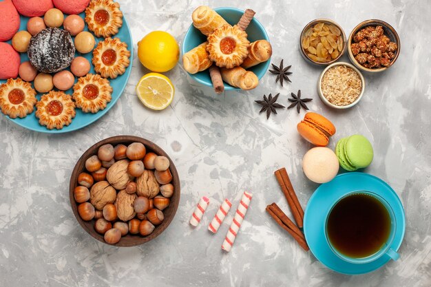 Vista superior de la taza de té con galletas, nueces y tortas rosas sobre superficie blanca