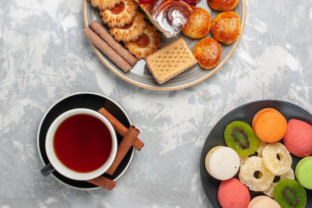 Vista superior de una taza de té con galletas y pasteles en la superficie blanca