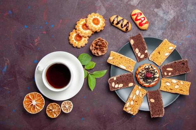 Vista superior de la taza de té con galletas y rebanadas de pastel en el espacio oscuro