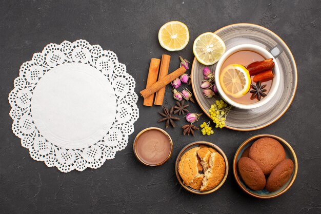 Vista superior de una taza de té con galletas y rodajas de limón en la superficie oscura, té, azúcar, fruta, galleta, galleta dulce